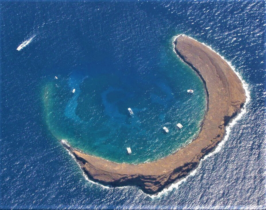 Aerial of the Molokini Crater of Maui with charter boats floating above the coral that lies beneath.
